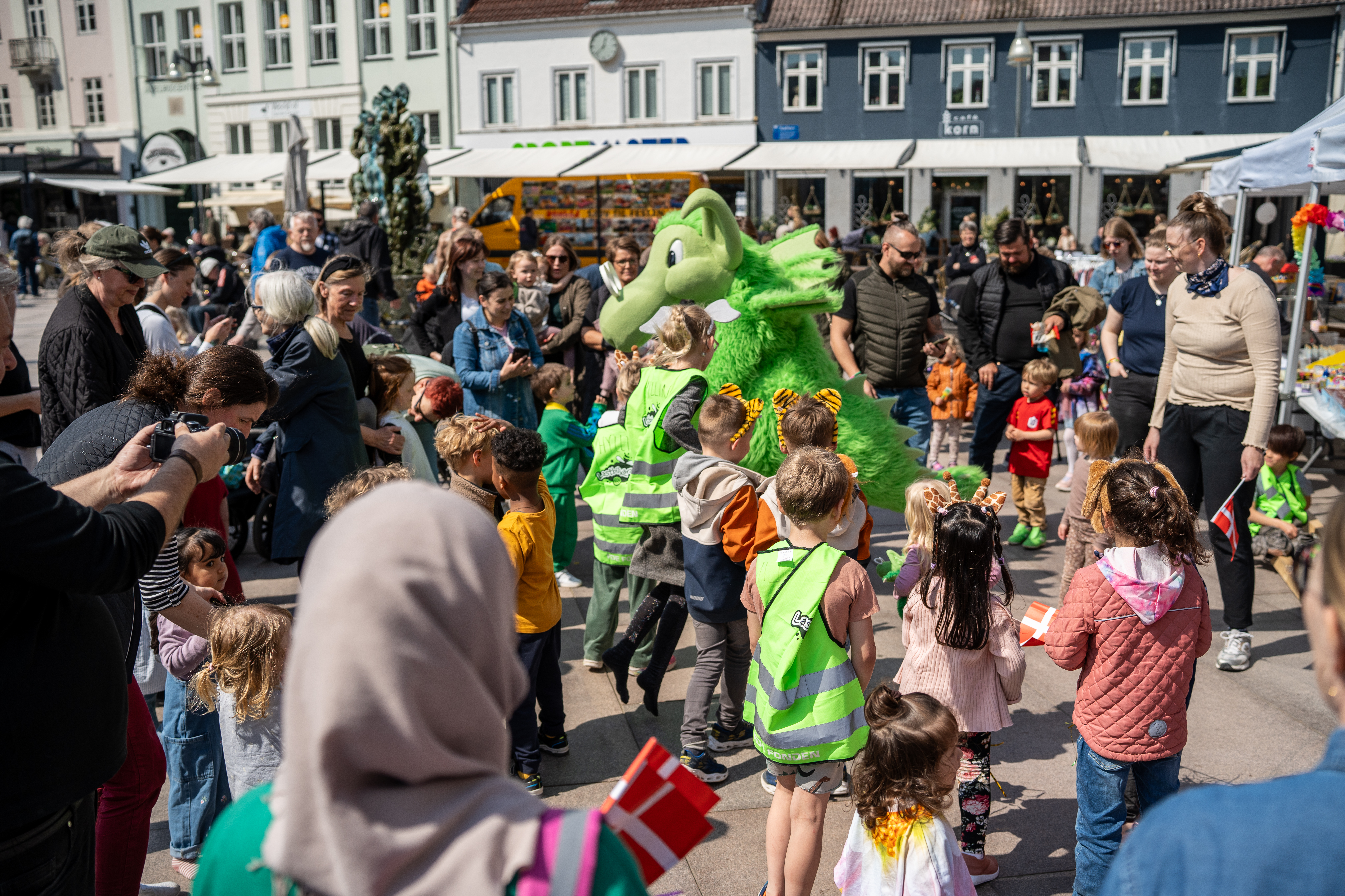 Børn og forældre står rundt om stor, grøn plysdrage, Næssi, på Axeltorv i Næstved. 