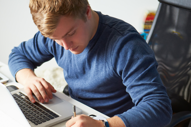 På billedet ses en mand ved en pc. Han noterer i en blok