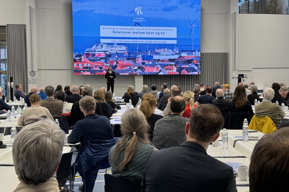 Mødedeltagere til stort møde kigger op mod skærm med præsentation