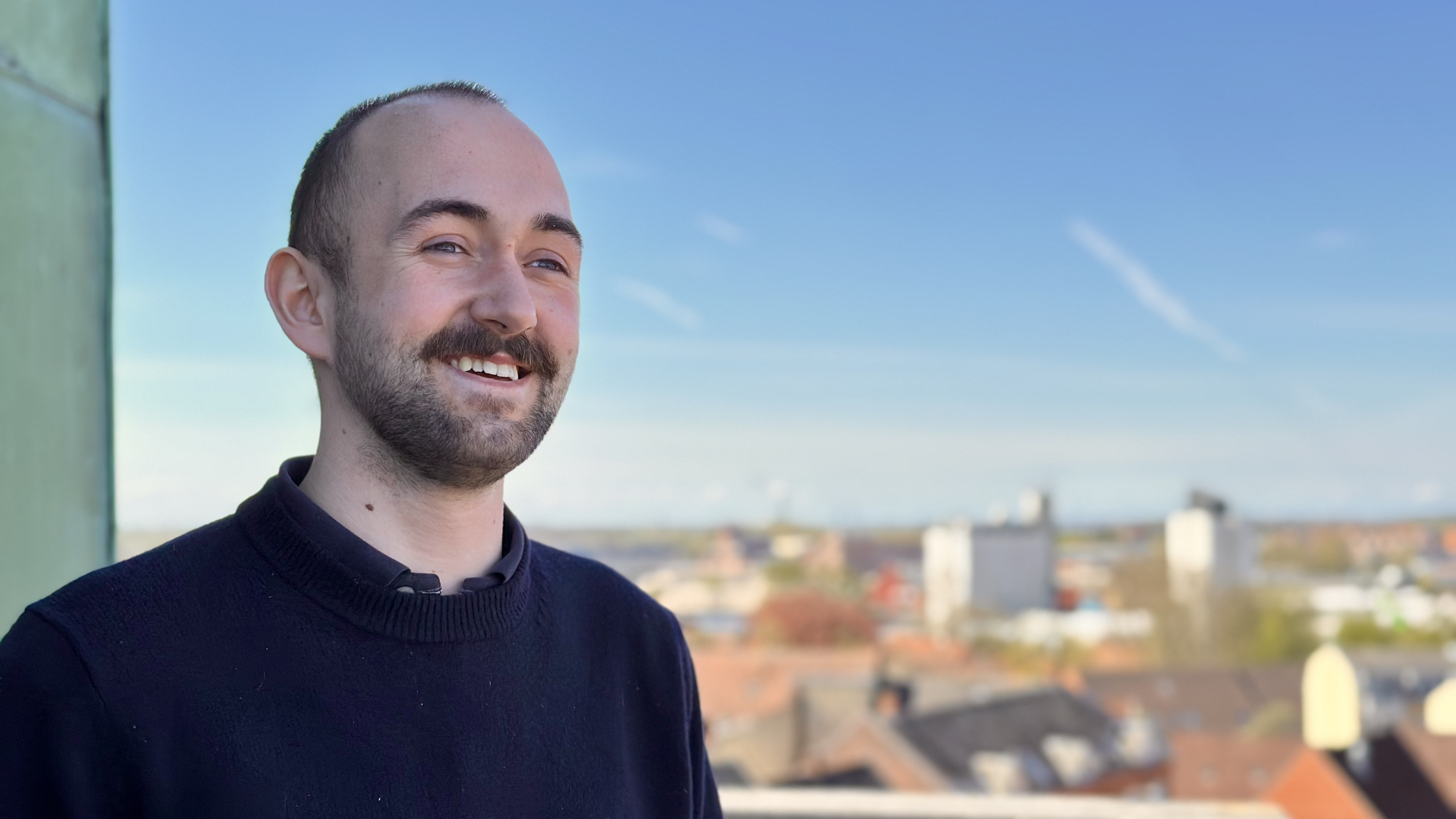 Mand smiler og kigger ud over Næstved by i baggrunden ses siloerne på havnen. 