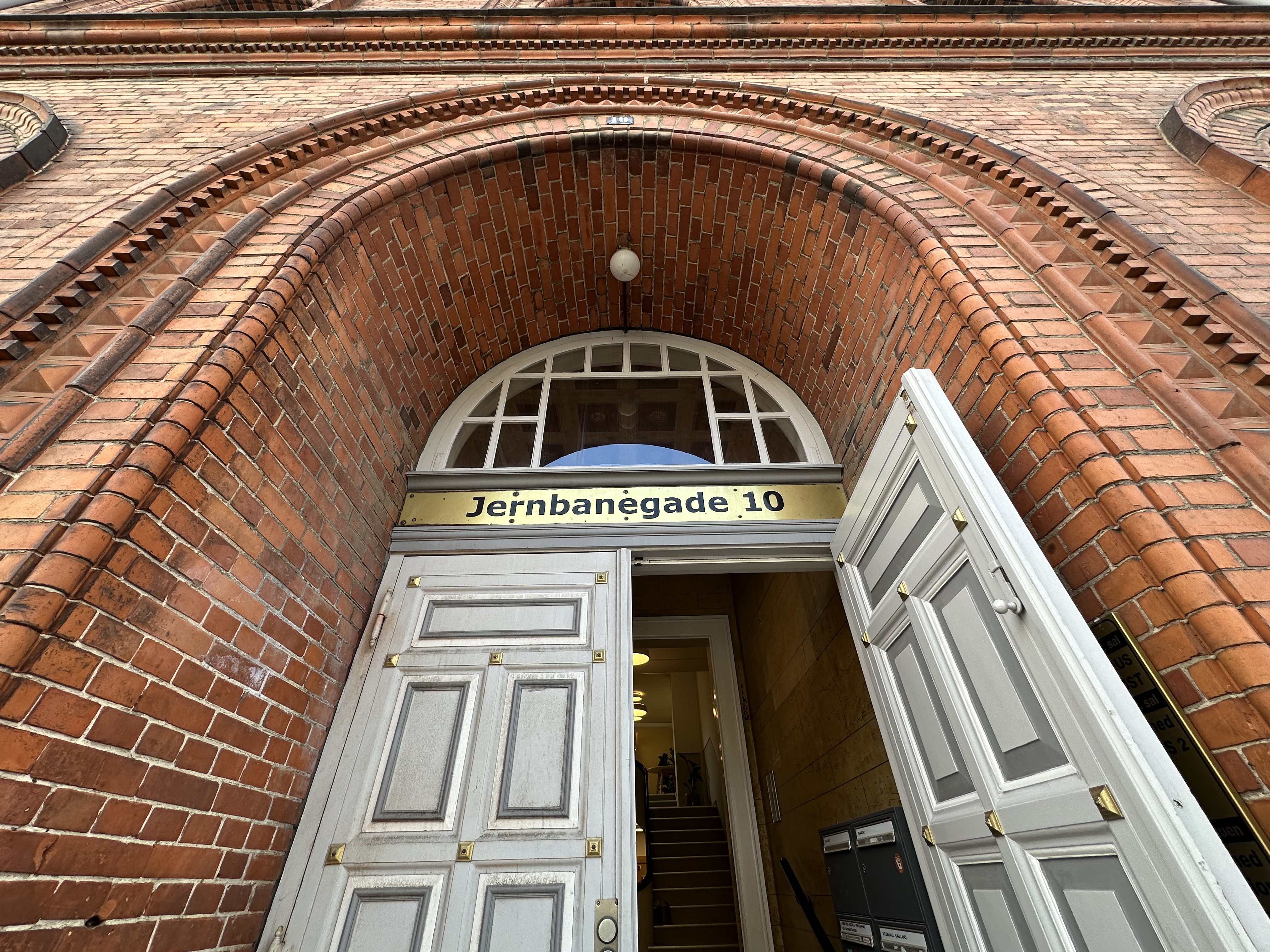 Indgangsdør til gammel murstenbygning, hvor der står Jernbanegade 10 på et guldskilt over døren. 