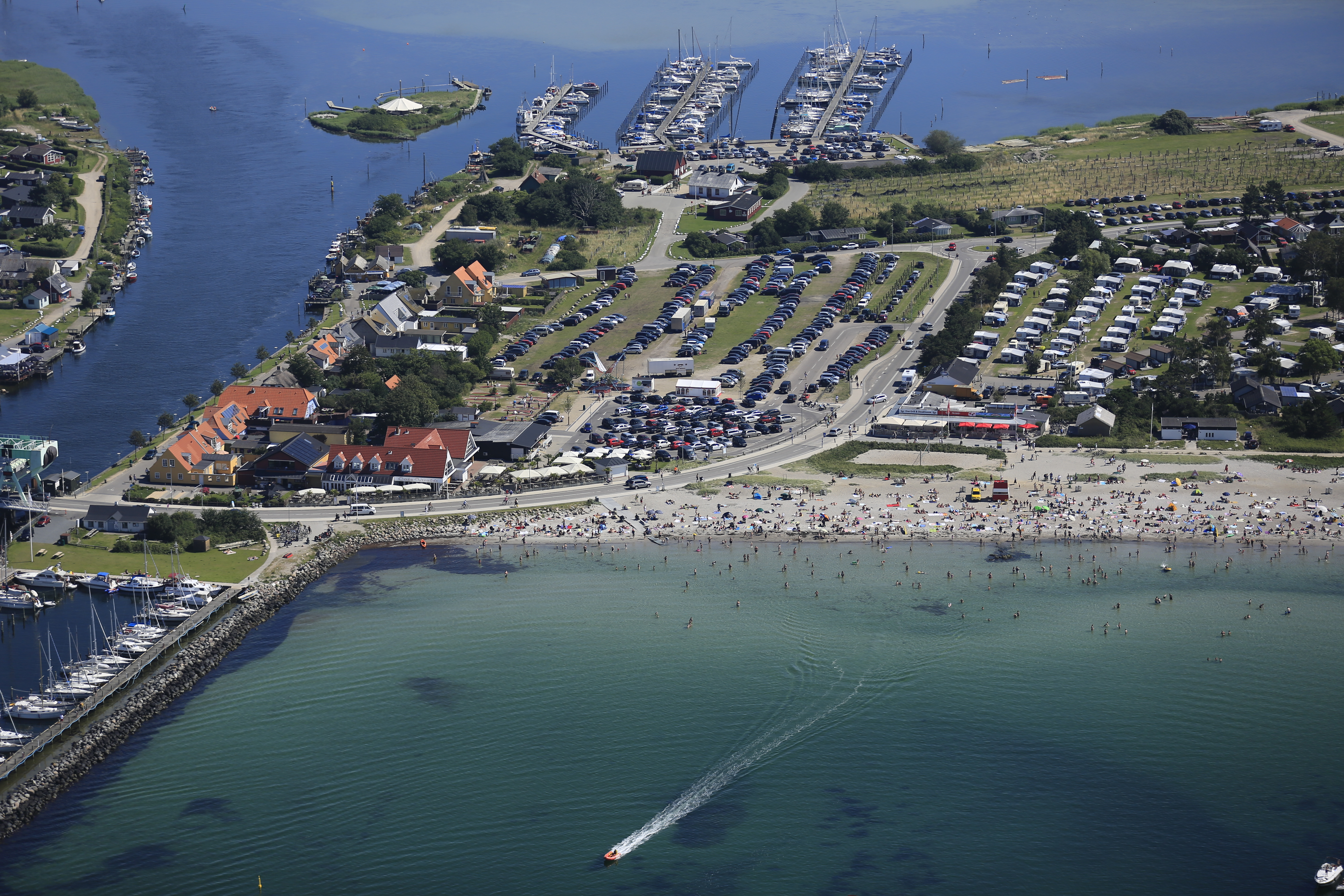 Dronebillede af badestrand, vand og en ø.