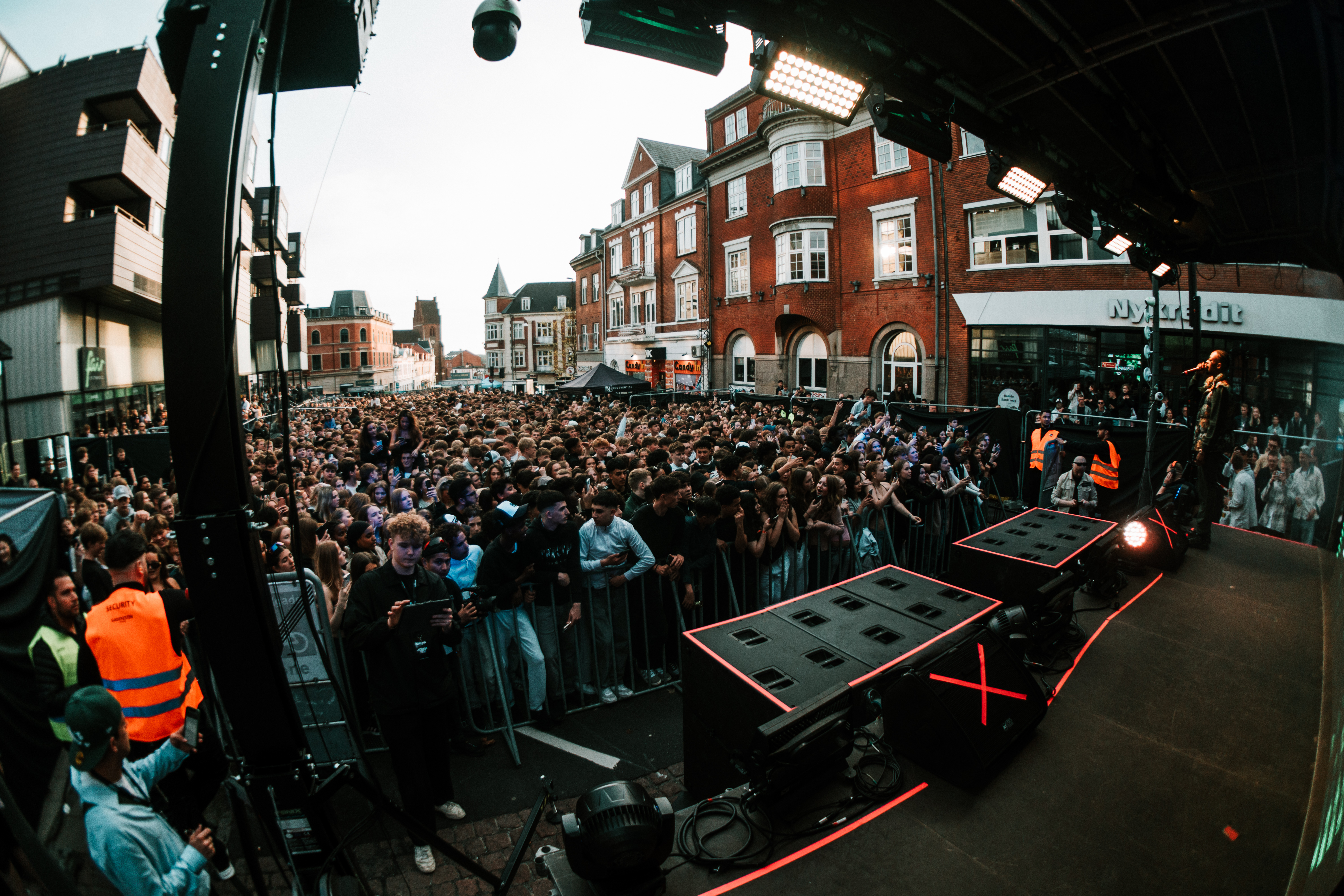 Billede taget fra en scene med højtalere i forgrunden og en stor menneskemængde i gaden i baggrunden. 