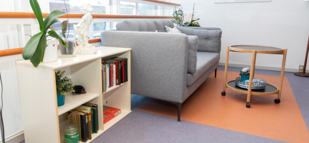 Sofaarrangement, grå sofa og hvid reol med bøger, rundt bord med sort plade