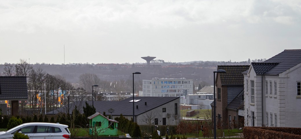 En bil holder parkeret ved hus, i baggrunden ses en tom legeplads og udsigt til vandtårnet i Næstved Nord