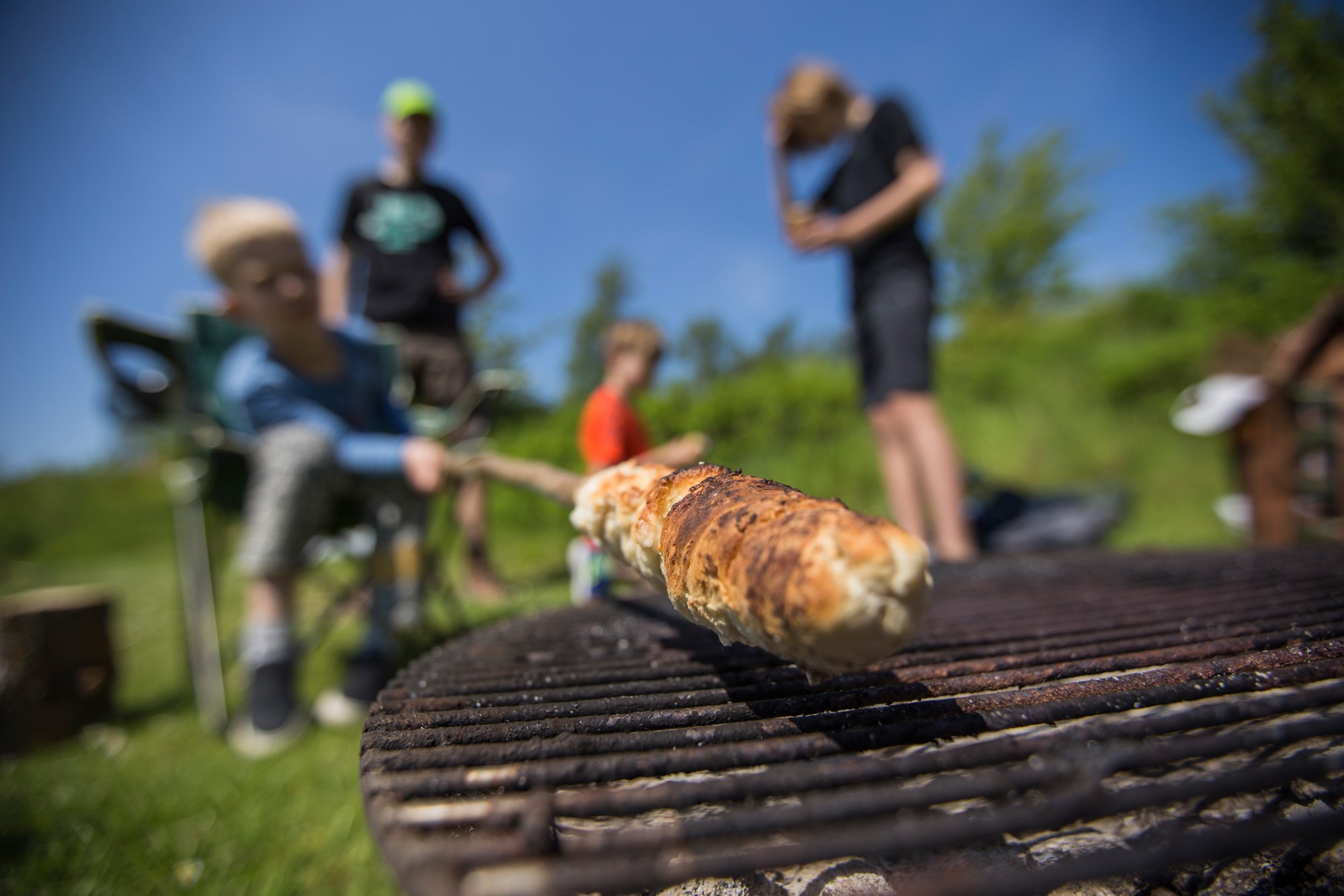En dreng holder snobrød over bål imens to andre drenge står bag ham 