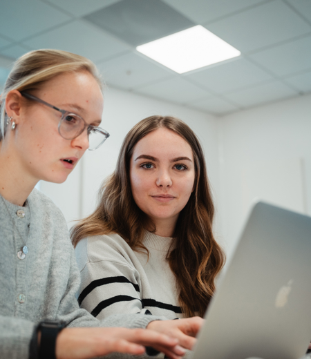 To piger snakker sammen om en opgave med hver deres computer To piger snakker sammen om en opgave med hver deres computer