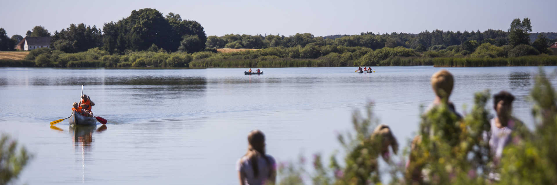 Person sejler i kano på sø i Næstved Kommune, mens folk kigger på