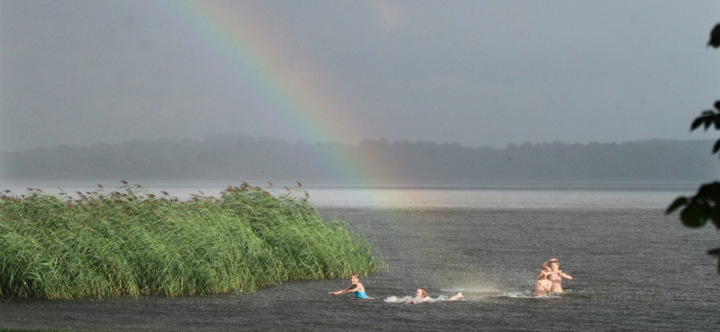 To piger leger i vandet imens en regnbue lyser op bag dem