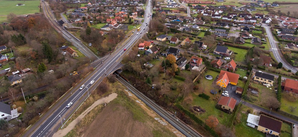 Dronefoto over Holme Olstrup hvor togskinner og landevej krydser igennem byen